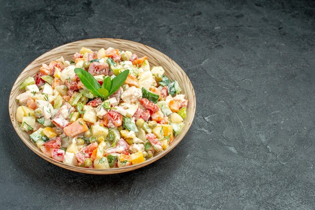 Side close view of bowl of vegetable salad on the left side with green on it on dark green background