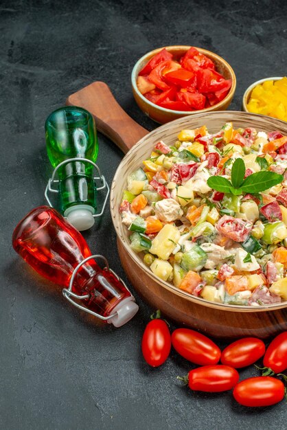濃い灰色の背景の側面に野菜とオイルビネガーボトルとプレートスタンドの野菜サラダのボウルの側面拡大図