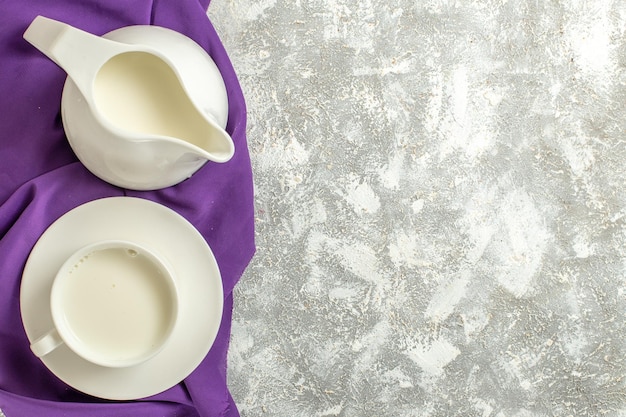 Side close view of a cup of milk and a jug of milk on a purple napkin at the side on a marble backgound Free Photo