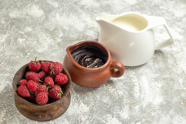 Side close view of a jug of chocolate jug of milk and bowl of raspberries on a marble background