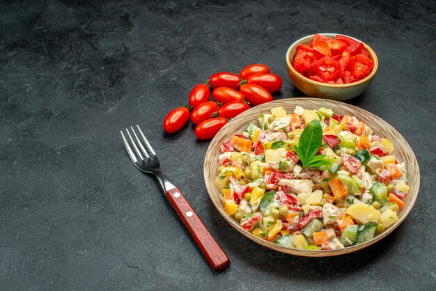 Side close view of vegetable salad with tomatoes and fork on dark grey background