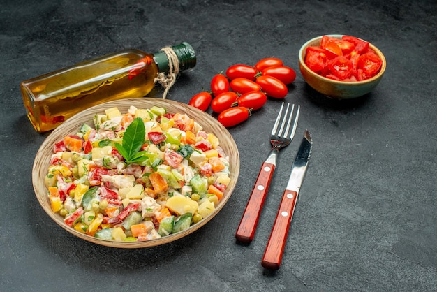 Side close view of vegetable salad with tomatoes oil bottle cutleries on side on dark grey background