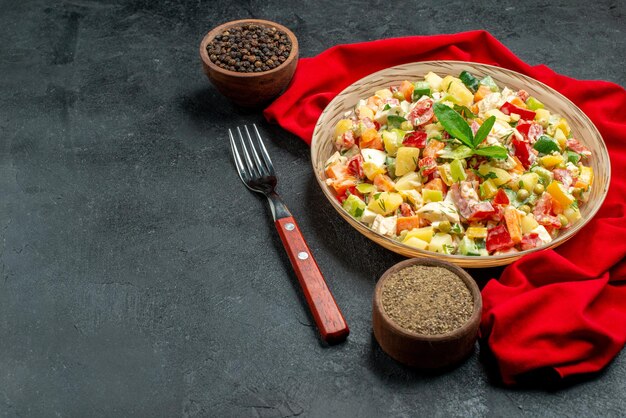 Side close view of veggie salad on red napkin with fork notepad and pepper on dark grey background