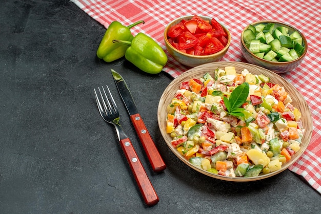 Side close view of veggie salad with vegetables and cutleries on side and red napkin on grey table