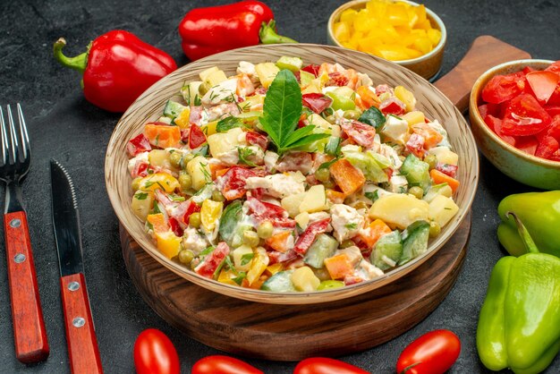 Side closest view of vegetable salad with cutleries and vegetables on side on dark grey background