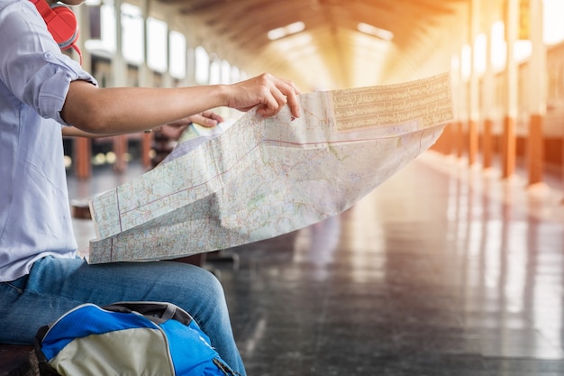 マップに座っている若い男性の旅行者の横の肖像画は、旅行する場所と列車を待っている鞄を選んで、ヴィンテージトーンフィルターを有効にした