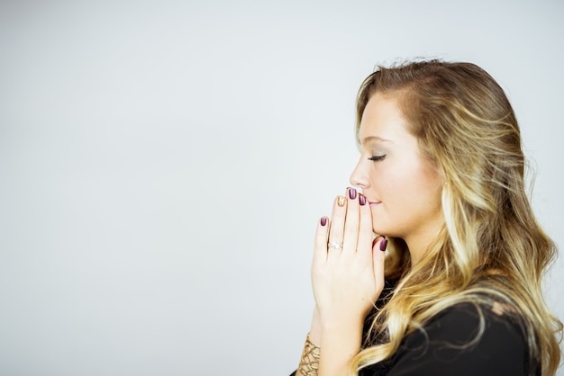 Free photo side profile of a praying blonde woman against a white