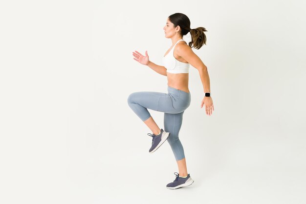 Side view of an active young woman running in place during a HIIT training. Sporty female athlete with a toned body doing a cardio workout