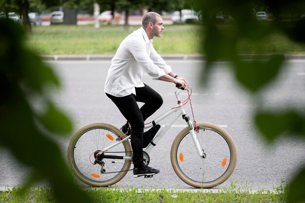 Foto gratuita bicicletta di guida del maschio adulto di vista laterale sulla via