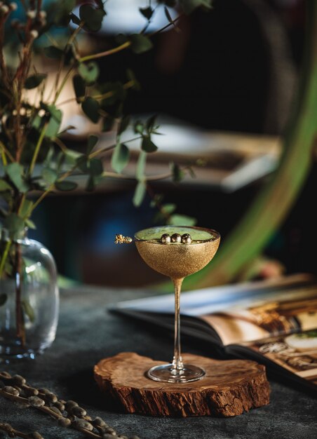 Вид сбоку алкогольного коктейля с киви в золотом бокале на деревянной подставке