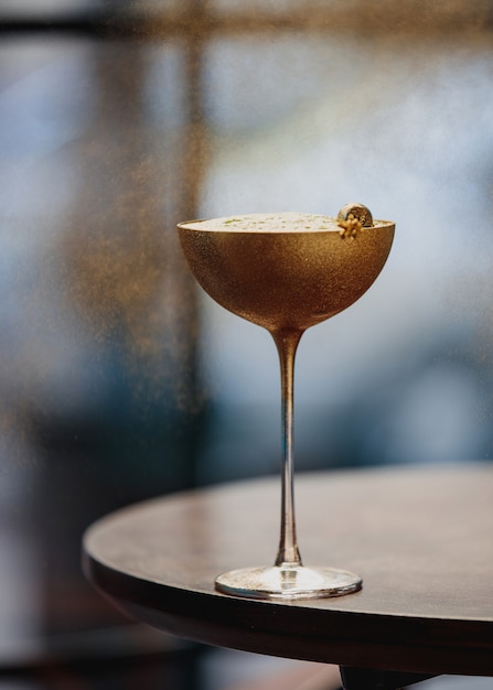 Вид сбоку алкогольного коктейля с киви в золотом бокале на деревянном столе