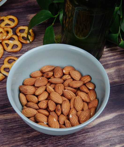 Side view of almond in a blue bowl and mini pretzels on rustic