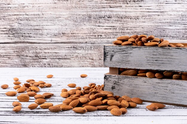 Side view almond in wooden box on white wooden table. horizontal