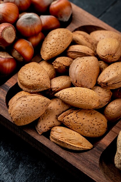 Side view of almonds in shell and hazelnuts on wooden background