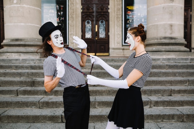 Free photo side view of a angry female mime pulling male mime suspender in front of stairway