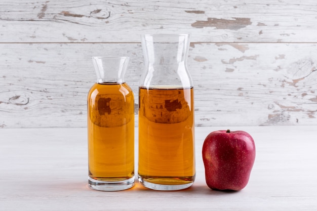 Вид сбоку яблочный сок на белом деревянном столе