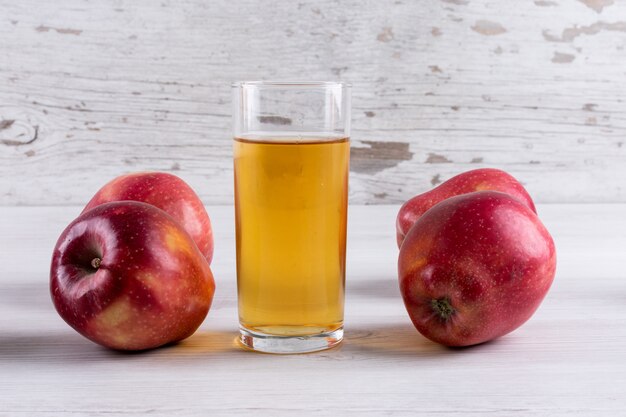 Side view apple juice with red apples on white wooden table