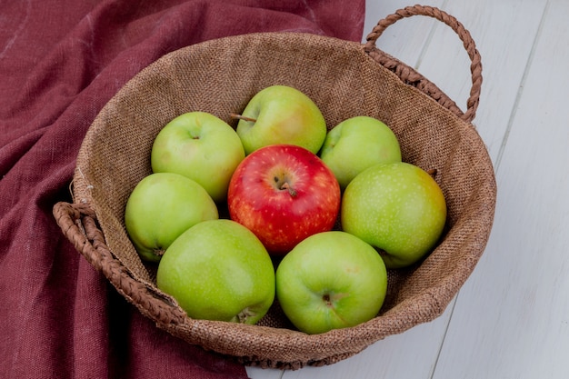 Side view of apples in basket on bordo cloth and wooden surface