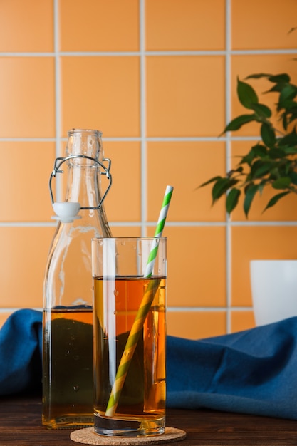 Side view apples in bottle and glass with apple juice on wooden and orange tile background. vertical