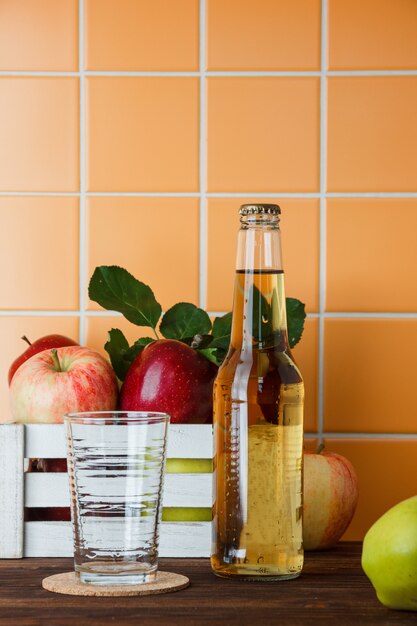 Side view apples in box with apple juice on wooden and orange tile background. vertical space for text