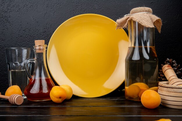 Side view of apricot compote and peach syrup with apricots and garlic crusher on wooden surface and black background