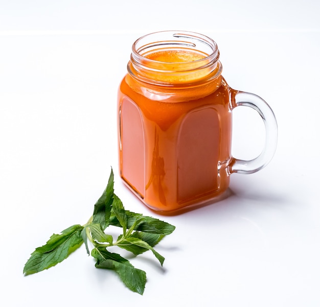 Side view of apricot smoothie in a glass jar with handle and mint on white surface