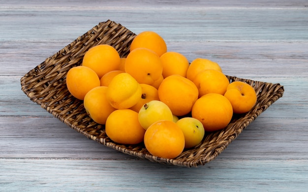 Side view of apricots in basket plate on wooden background