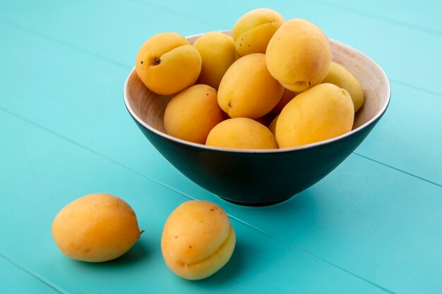 Side view of apricots in a bowl on a blue surface