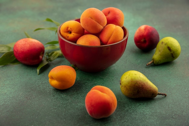 Side view of apricots in bowl with pattern of peaches pears and apricots on green background