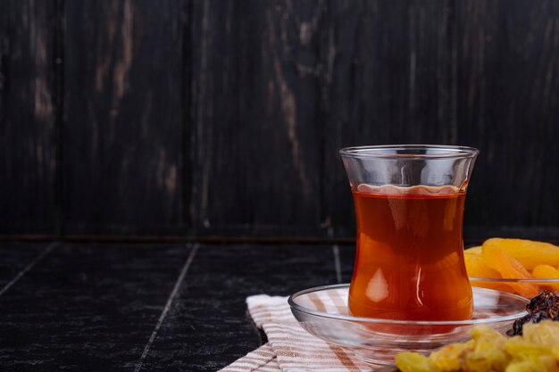 Side view of armudu glass of tea with dried fruits on black rustic background