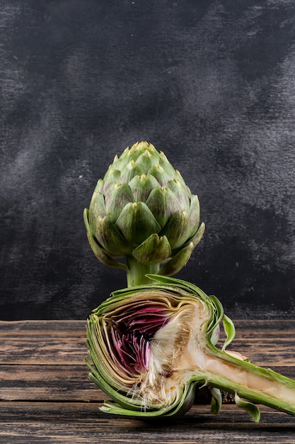 Free photo side view artichoke and a slice on dark wooden and black background. horizontal space for text
