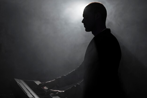 Вид сбоку художника, играющего на пианино с эффектами дыма и теней