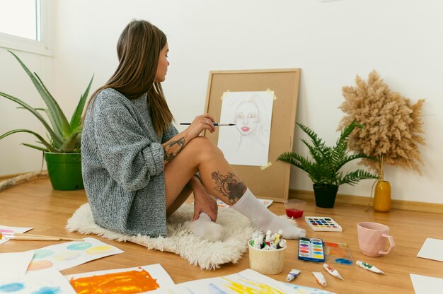 Side view artist sitting on the floor and painting on canvas