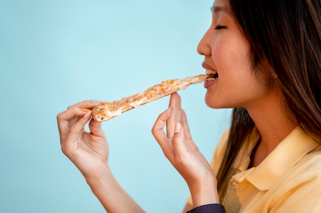 Вид сбоку азиатская женщина ест кусок пиццы