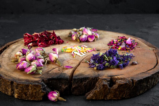 Side view of assortment of dry flower and rose tea on wooden board on black