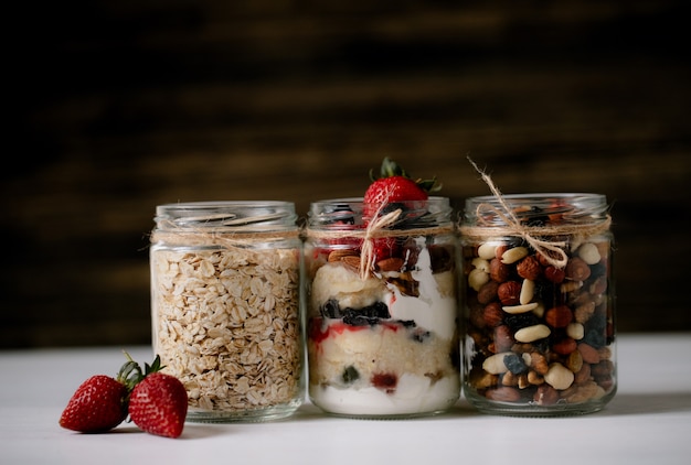 Side view of assortment overnight oats oat flakes and mixed nuts in glass jars on rustic table