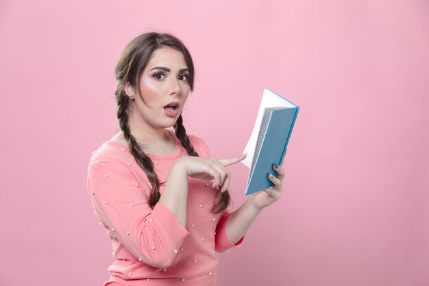 Free photo side view of astonished woman pointing at the book she's holding