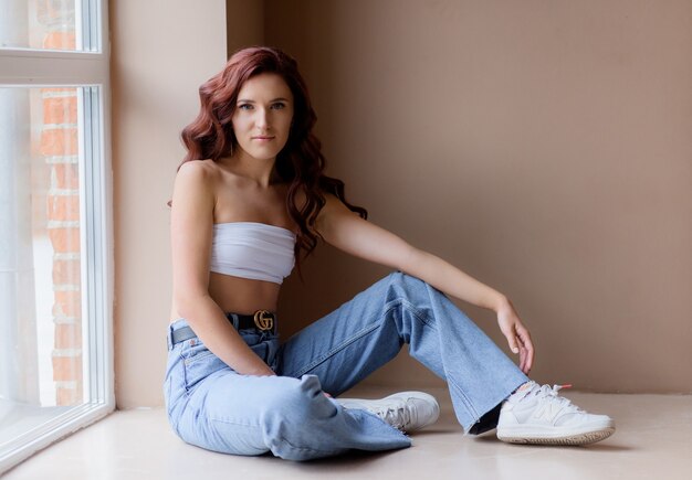 Side view of athletic girl sitting by the window and looking at the camera.