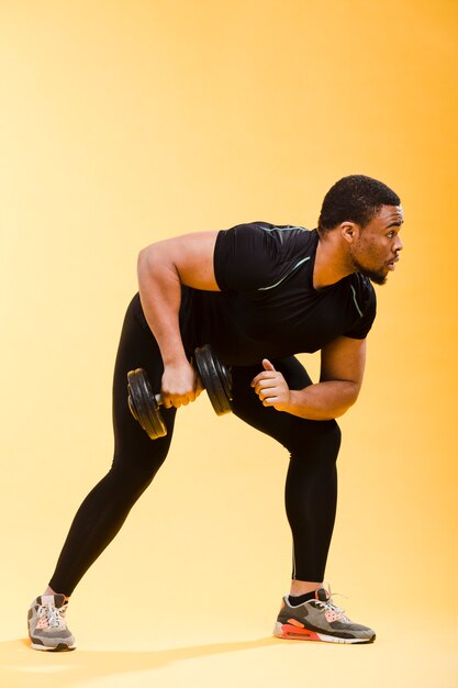 Side view of athletic man in gym outfit holding weights