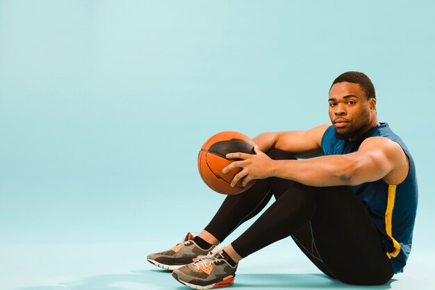 Side view of athletic man in gym outfit posing with basketball