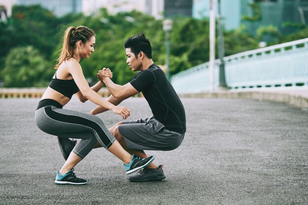 Side view of athletic man and woman doing one leg squat together outdoors