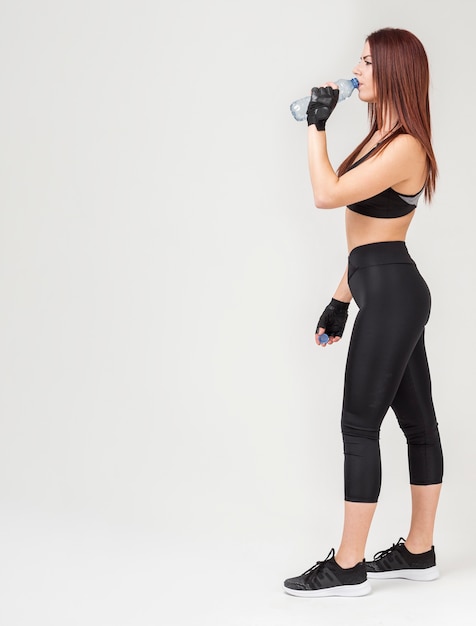 Side view of athletic woman in gym attire drinking water