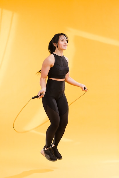 Side view of athletic woman in gym outfit jumping rope