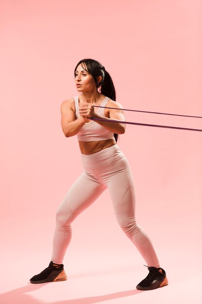 Side view of athletic woman in gym outfit pulling resistance band