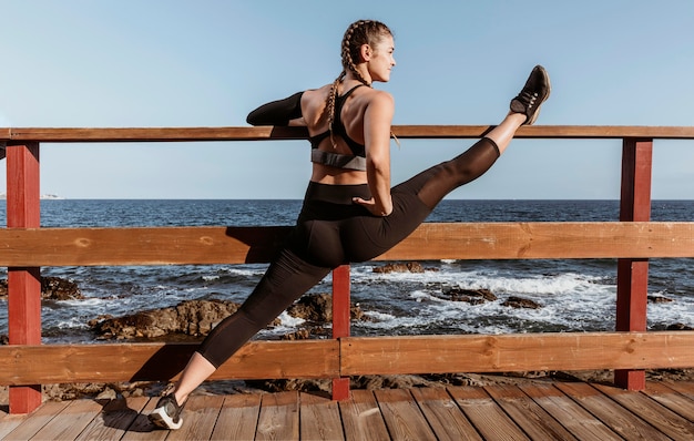 Free photo side view of athletic woman stretching by the beach
