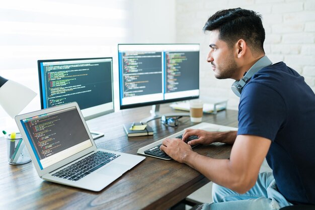 집에서 일하는 동안 컴퓨터를 사용하여 프로그래밍하는 매력적인 히스패닉 소프트웨어 개발자의 측면 보기