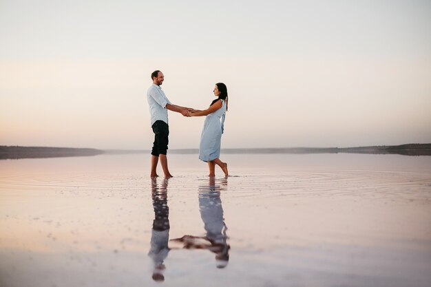 Side view of attractive young couple holding on their hands and standing on the beach