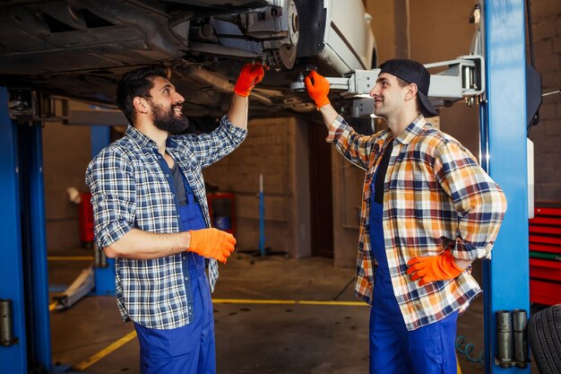 Side view of auto mechanics standing at lifted car in garage