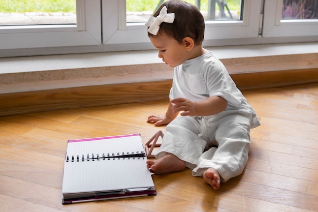 Side view baby sitting on floor with notebook