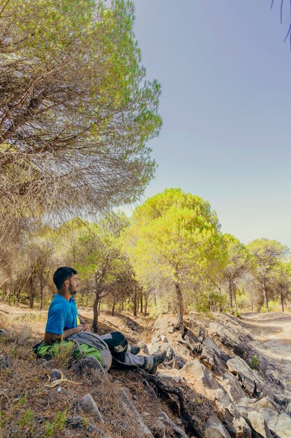 Side view of backpacker sitting under trees